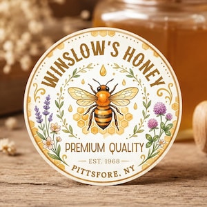 Peut inclure: Un autocollant circulaire illustrant une abeille au centre, entourée de brins de lavande et de trèfle. Le texte indique WINSLOW'S HONEY, PREMIUM QUALITY, EST. 1968 et PITTSFORE, NY. Le motif inclut un alvéole et des bordures dorées décoratives.
