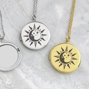 Puede incluir: Tres medallones redondos con diseños celestiales. Un medallón está abierto, revelando el interior. Los otros dos medallones están cerrados, uno plateado y otro dorado. Cada medallón presenta un diseño de sol y luna con una cara.