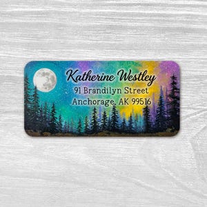 May include: A rectangular address label featuring a colorful night sky with a full moon and silhouettes of pine trees. The text reads Katherine Westley, 91 Brandilyn Street, Anchorage, AK 99516 in black script and serif fonts against a gradient background.