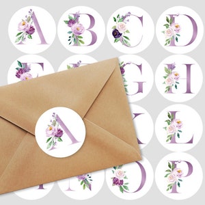 May include: A brown envelope with a circular sticker featuring the letter "A" in lavender, adorned with watercolor flowers in shades of purple and white. Additional stickers with various letters and floral designs are visible.