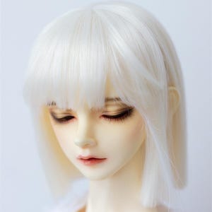 May include: A white doll with a short, straight, white wig with bangs. The doll is wearing a white shirt.