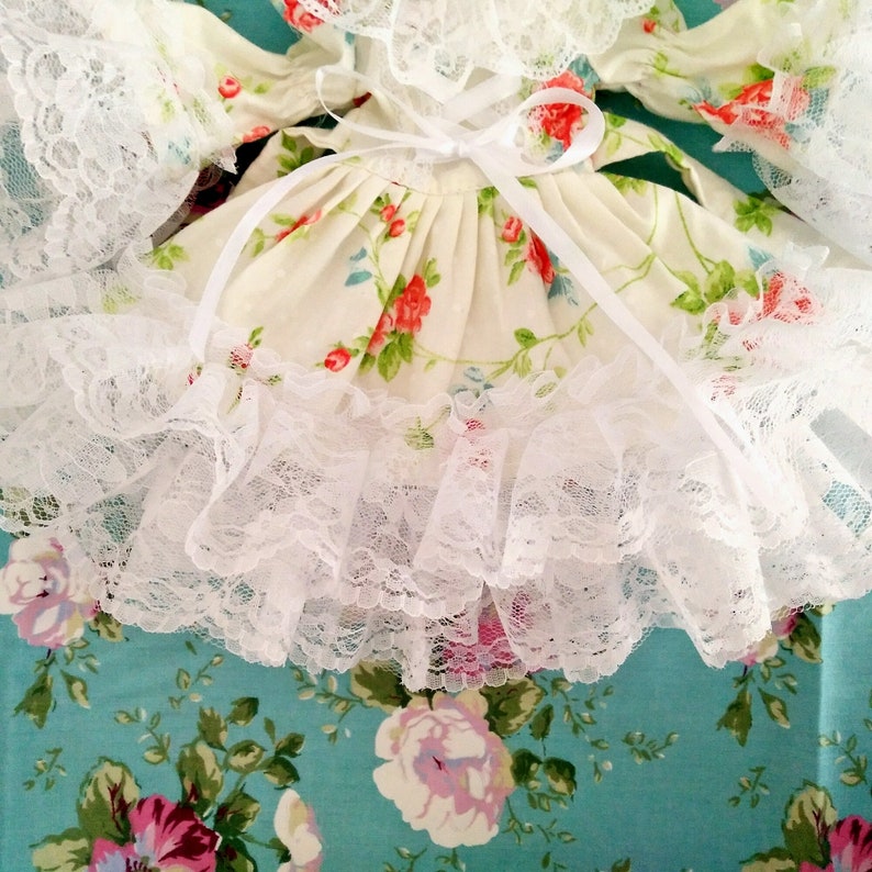 May include: A white lace dress with a floral print and a white satin ribbon tied at the waist.