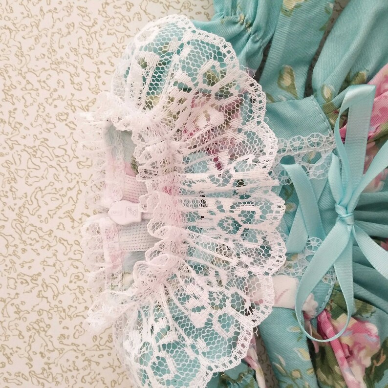 May include: A light blue dress with a white lace trim and a matching light blue ribbon bow. The dress has a floral print with pink and white flowers.