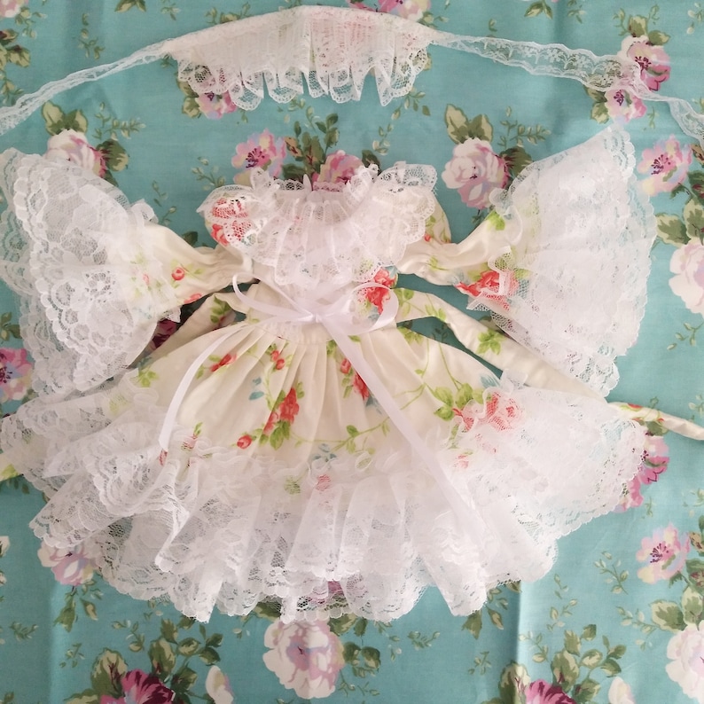 May include: A white lace dress with a floral print and a white satin ribbon. The dress has a ruffled hem and lace sleeves.