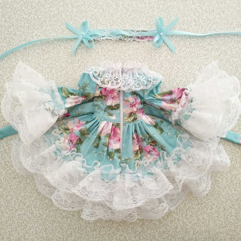 May include: A light blue dress with a floral print and white lace trim. The dress has a zipper closure in the back and a white lace collar.