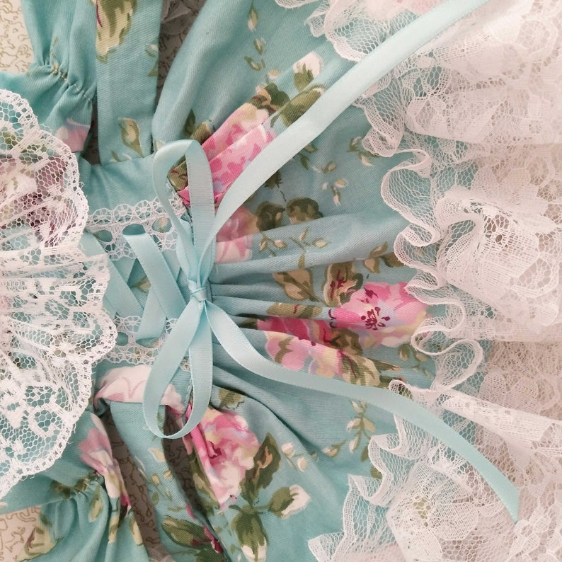 May include: A light blue dress with a floral print and white lace trim. The dress has a bow at the back and is tied with a light blue ribbon.