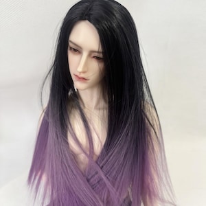 May include: A doll with black hair that fades to purple at the ends. The doll has a pale complexion, red-toned lips, and is looking down. The doll's hair is long and straight, and the background is a plain white.
