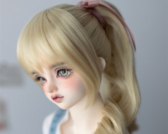 May include: A doll with long, blonde hair styled in a ponytail with a pink ribbon. The doll has blue eyes and is wearing a light blue and white outfit.