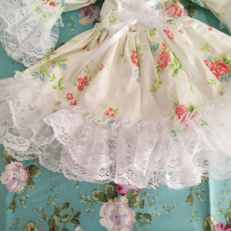 May include: A white dress with a floral print and white lace trim. The dress has a white ribbon tied at the waist.