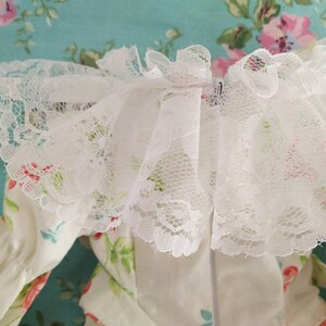 May include: White lace trim with a ruffled edge. The lace is delicate and has a floral pattern. The trim is perfect for adding a touch of elegance to any garment.