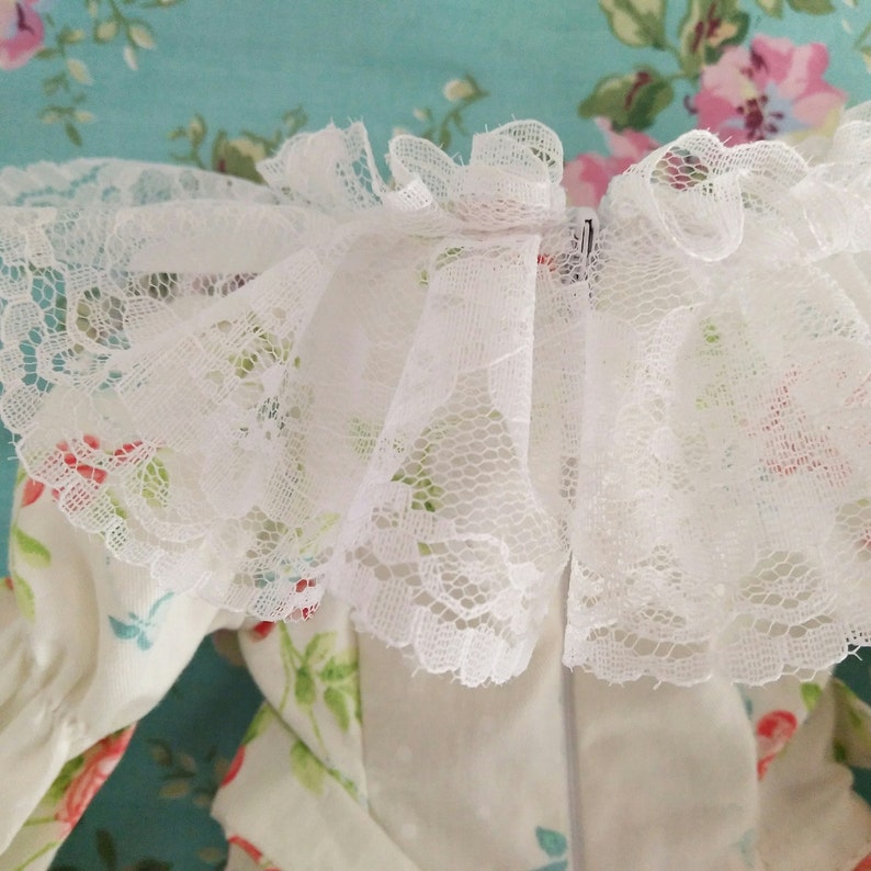May include: White lace trim with a ruffled edge. The lace is delicate and has a floral pattern. The trim is perfect for adding a touch of elegance to any garment.