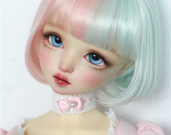 Può includere: Una bambola con capelli rosa e blu chiaro, che indossa un vestito rosa con pizzo bianco e un nastro rosa intorno al collo.