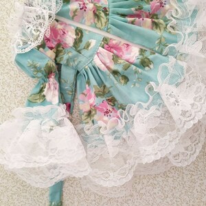 May include: A light blue dress with a floral print and white lace trim. The dress has a zipper closure and a tie at the back.
