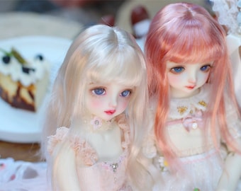 May include: Two dolls with long hair, one with white hair and blue eyes and the other with pink hair and blue eyes. Both dolls are wearing white dresses with lace details.