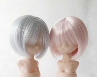 Peut inclure: Deux têtes de poupées avec des perruques courtes et lisses. L'une est gris argenté clair, l'autre rose pâle. Les poupées sont montées sur des socles, sur fond blanc. Les perruques ont une texture lisse.
