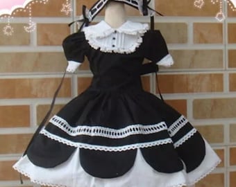 May include: A black and white dress with a white lace collar and trim. The dress has a full skirt with a scalloped hem and a black ribbon tied around the waist.