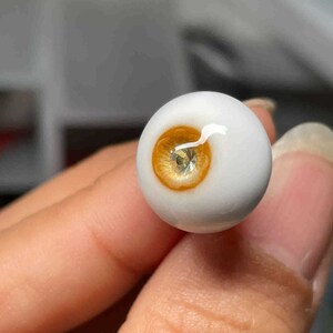 Op de afbeelding: Een close-up van een wit poppenoog met een gele iris en een helder, glanzend oppervlak.