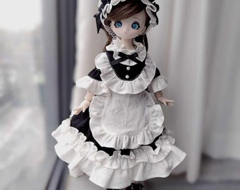 May include: A doll dressed in a black and white maid outfit, complete with a ruffled apron and matching bonnet. The doll has large blue eyes and black shoes. The outfit features a black bow and decorative buttons.