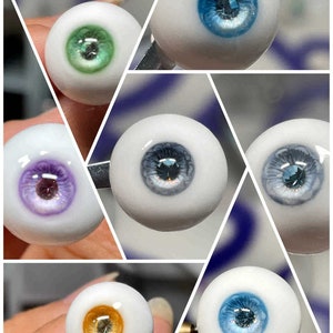 Op de afbeelding: Een verzameling van zes verschillende gekleurde glazen ogen met een witte basis en een donkerblauwe iris. De ogen zijn gerangschikt in een raster.