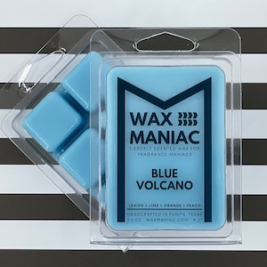 May include: A blue wax melt in a clear plastic container with the text "WAX MANIAC" and "BLUE VOLCANO" on the label. The label also includes the scent notes "LEMON + LIME + ORANGE + PEACH" and the text "HANDCRAFTED IN PAMPA, TEXAS 2.5 OZ WAXMANIAC.COM # 37".