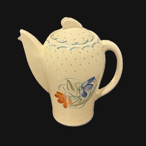 May include: Cream-coloured ceramic teapot with a lid and handle. The teapot is decorated with blue dotted patterns and a floral design featuring orange and blue flowers. The spout is long and curved.
