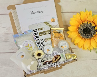 May include: A gift box filled with self-care items, including bath salts, hand lotion, foot pack, chocolates, and a sunflower. The box contains a card that reads "A little something just for you". The theme is relaxation and pampering.