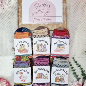 May include: A festive gift box containing several pairs of patterned socks. Each pair is labelled with a name and the words "Cozy Lounge Socks" or "Reading Socks". The box itself has the text "Something just for you Merry Christmas". The socks feature various colors and designs.