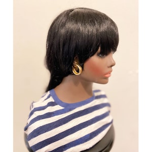 May include: A black wig with blunt bangs and a side part. The wig is styled on a mannequin wearing a blue and white striped shirt.