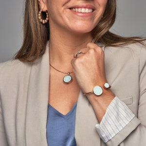 Könnte beinhalten: Ein roségoldenes Halsketten- und Armbandset mit einem hellblauen runden Anhänger und einem Manschettenarmband. Anhänger und Manschette tragen beide das Wort "LOVE" auf sich.