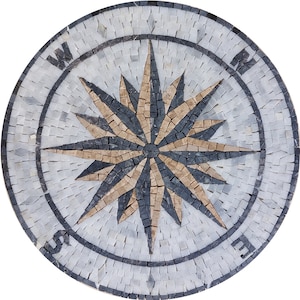Op de afbeelding: Een witte marmeren kompasmozaïek met een zwart en bruin sterontwerp. De kompaspunten zijn gemarkeerd met de letters N, S, E en W.