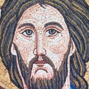 May include: Close-up of a mosaic portrait depicting a man with a beard and long hair. The mosaic is composed of small, rectangular tiles in shades of brown, beige, and blue. The man's face is detailed, with a serene expression.