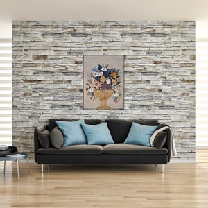 May include: A floral arrangement in a gold vase, with a variety of flowers in shades of pink, white, yellow, and orange. The arrangement is displayed on a beige wall with a stone texture.