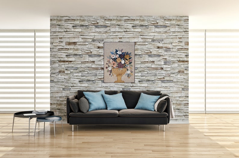 May include: A floral arrangement in a gold vase, with a variety of flowers in shades of pink, white, yellow, and orange. The arrangement is displayed on a beige wall with a stone texture.