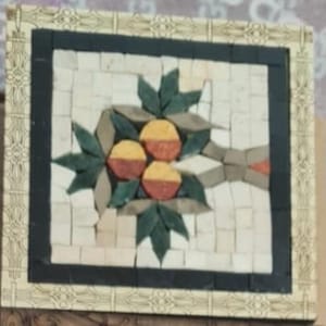 Könnte beinhalten: Quadratische Mosaikfliesen-Kunst mit einem Fruchtdesign. Das Mosaik hat einen cremefarbenen Hintergrund mit einem schwarzen Rand. Die Frucht ist mit gelben und roten Segmenten dargestellt, umgeben von grünen Blättern und geometrischen Formen.