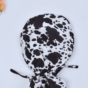 May include: A black and white cow print surgical scrub hat with ties.