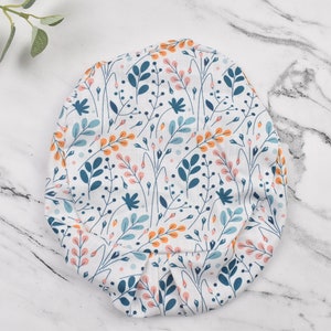 Puede incluir: Un gorro de quir&oacute;fano de tela blanca con un patr&oacute;n floral con flores y hojas azules, naranjas y rosas.