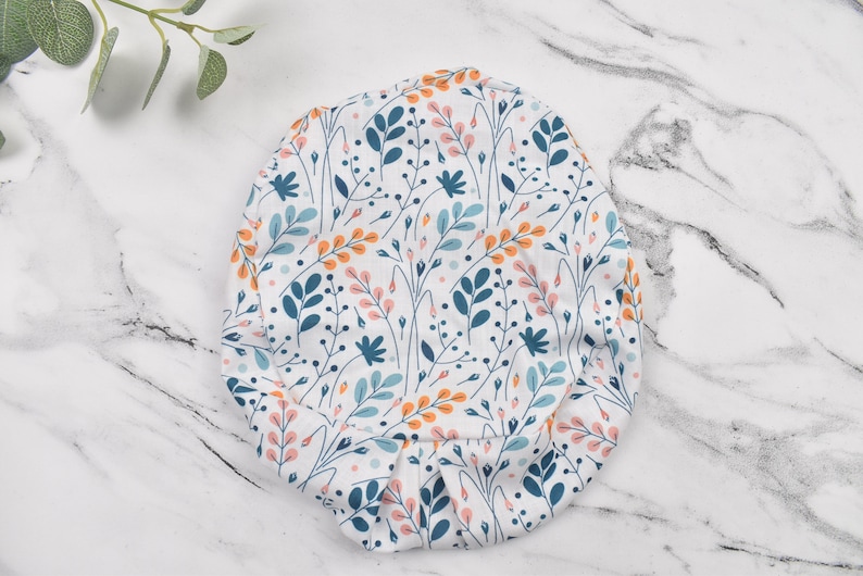 Puede incluir: Un gorro de quir&oacute;fano de tela blanca con un patr&oacute;n floral con flores y hojas azules, naranjas y rosas.