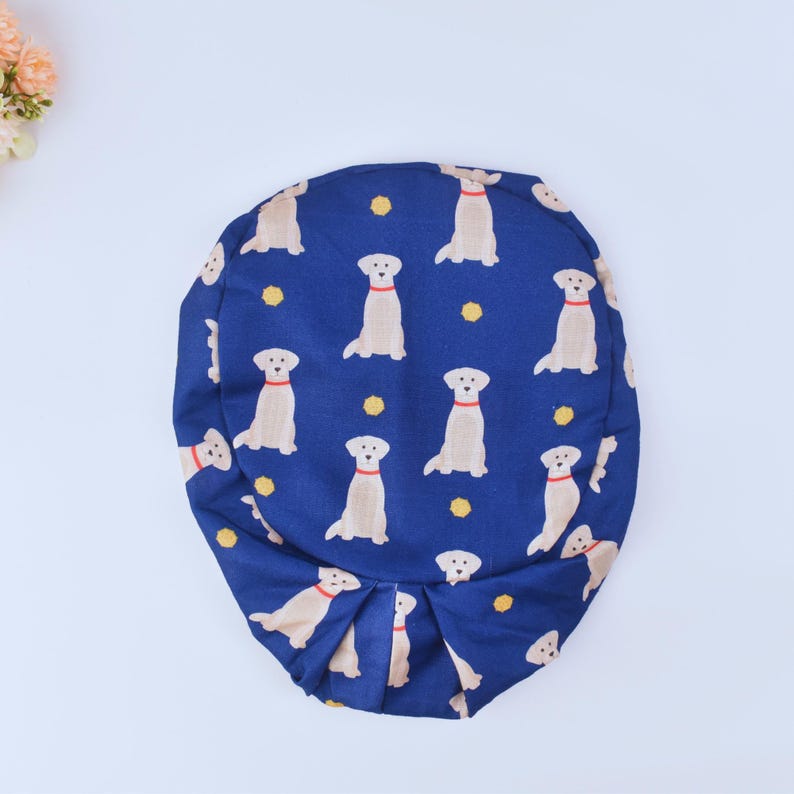 May include: A blue fabric cushion with a pattern of yellow Labrador Retrievers. The cushion is round and has a gathered edge.
