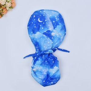 May include: A blue fabric scrub hat with a white galaxy print featuring stars, planets, and a crescent moon.