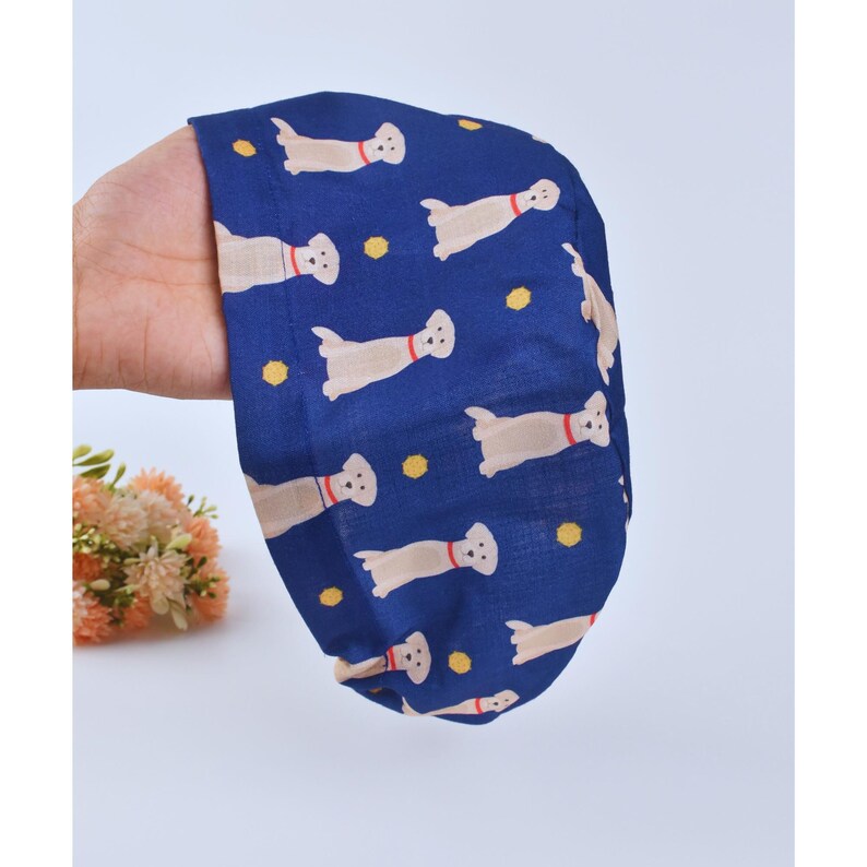 May include: A blue scrub hat with a pattern of white dogs and yellow dots.