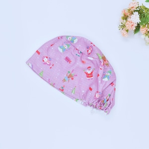 May include: A lilac surgical scrub cap adorned with a Christmas-themed design. The pattern includes Santa Claus, snowmen, reindeer, and presents. The cap is made from a soft, lightweight fabric, suitable for medical staff or anyone seeking a festive accessory for the holidays.