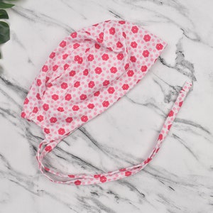 May include: A pink and white surgical scrub cap with a floral pattern. The cap has two long ties that can be tied at the back of the head.