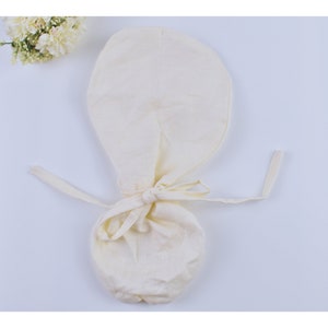 May include: A white cotton baby bonnet with a gathered top and a tie closure. The bonnet is made of soft, breathable fabric and is perfect for keeping a baby's head warm and protected.