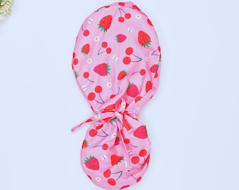 Peut inclure: Un bonnet de chirurgien rose avec un imprimé de fraises et de cerises. Le bonnet a une cravate à l'arrière.
