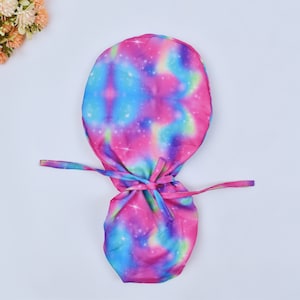 May include: A pink, blue, and green tie-dye surgical scrub hat with a galaxy print. The hat has a drawstring closure.