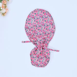 Könnte beinhalten: Ein Haargummi aus Stoff mit pinkfarbenem und grünem Blumendruck, einem gerafften Oberteil und zwei langen Bändern.