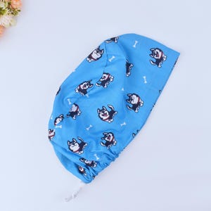May include: A blue surgical scrub hat with a pattern of black and white cartoon dogs and white bones.