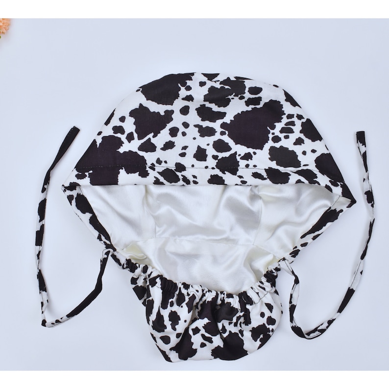 May include: A black and white cow print satin sleep cap with a white satin lining and adjustable ties.