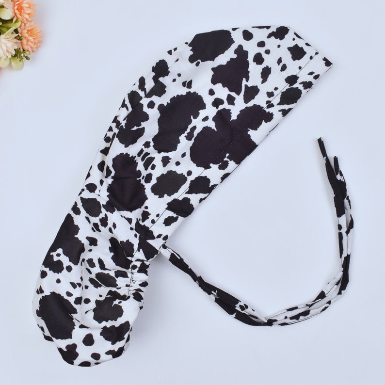 May include: A black and white cow print surgical scrub hat with a drawstring tie.