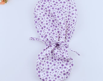 May include: A white surgical cap with a purple floral pattern. The cap is tied at the back with two long ties.